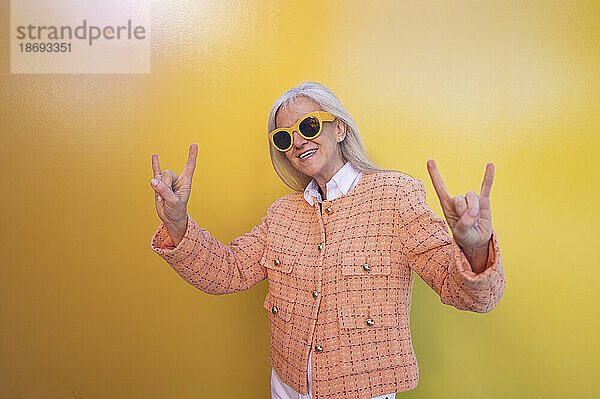 Frau mit Sonnenbrille macht vor der Wand ein Hupenschild