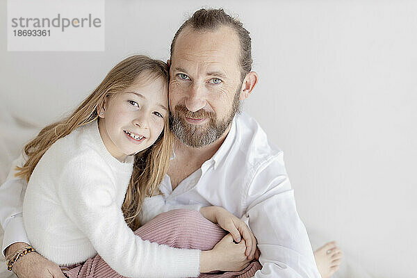 Father and daughter sitting near white wall