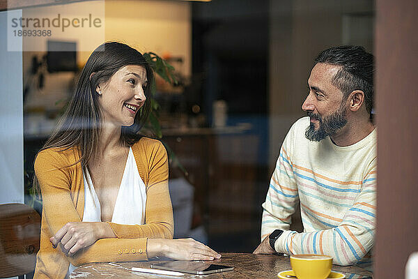 Ein Paar redet miteinander und sitzt im Café  gesehen durch die Glasscheibe