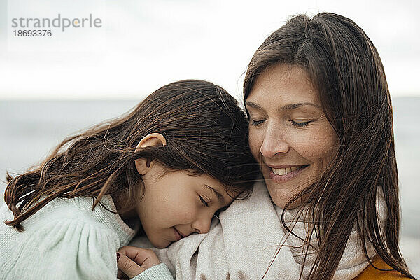 Lächelnde Frau umarmt Tochter am Strand