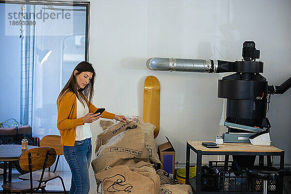 Frau nimmt per Smartphone im Café eine Bestandsaufnahme der Kaffeebohnen vor