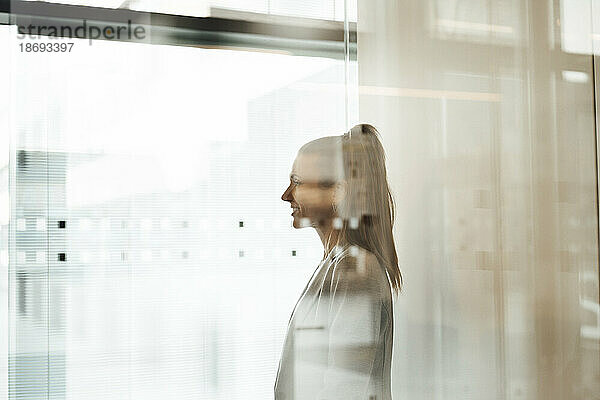 Smiling businesswoman at office seen through glass wall