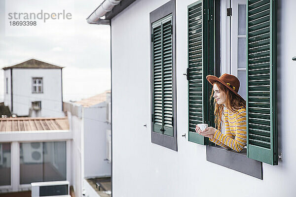 Frau mit Tasse in der Hand lehnt am Fenster