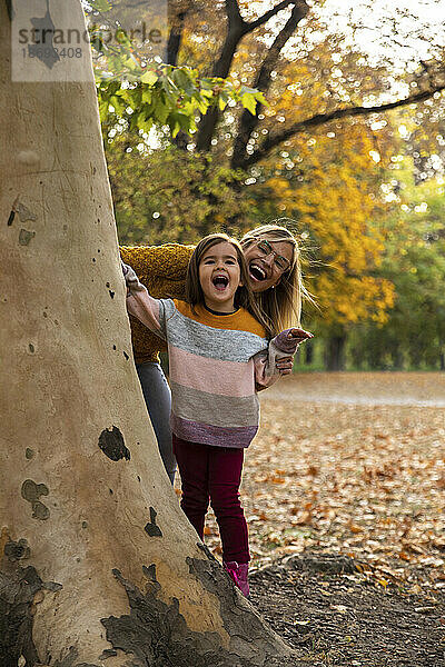 Fröhliche Mutter und Tochter stehen hinter einem Baum