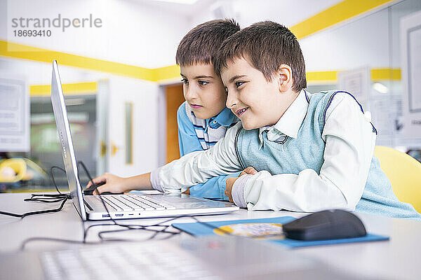 Lächelnder Junge teilt Laptop mit Freund im Computerunterricht in der Schule