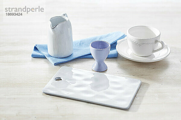 Studio shot of empty milk jug  cup  cutting board  napkin and eggcup