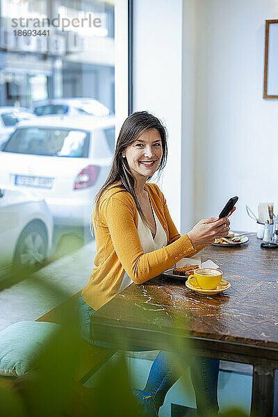 Lächelnde Frau mit Smartphone sitzt im Café