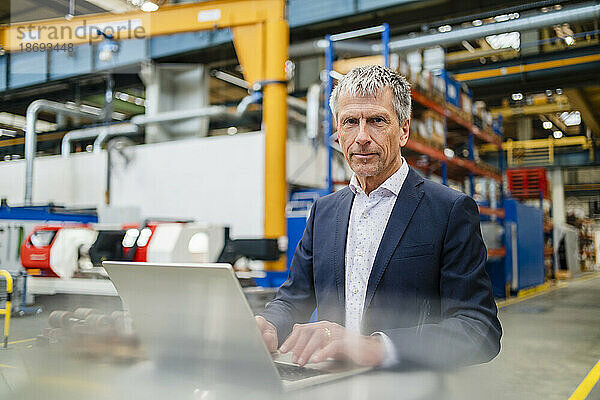 Geschäftsmann im Anzug am Laptop in der Fabrik