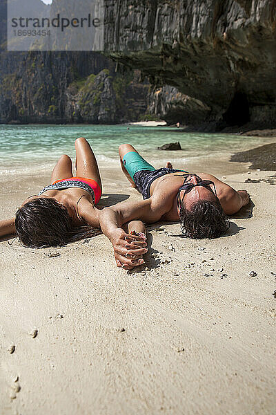 Freund und Freundin liegen Händchen haltend im Sand am Strand