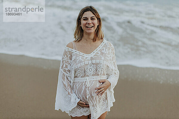 Glückliche schwangere Frau  die am Strand steht