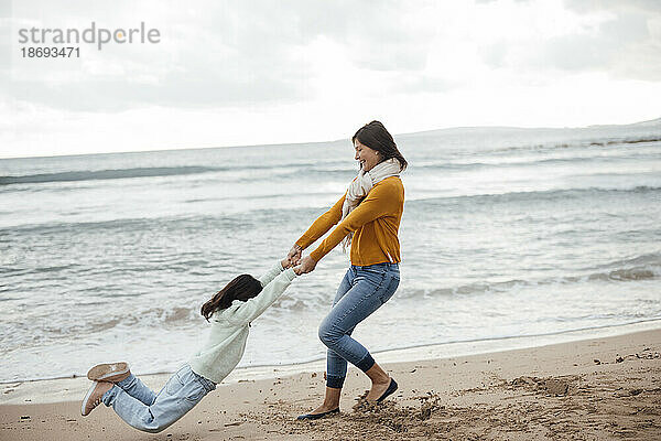 Glückliche Frau spinnt Tochter am Strand