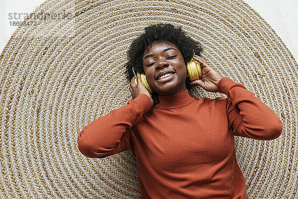 Glückliche junge Frau mit geschlossenen Augen  kabellosen Kopfhörern und auf einem Teppich liegend