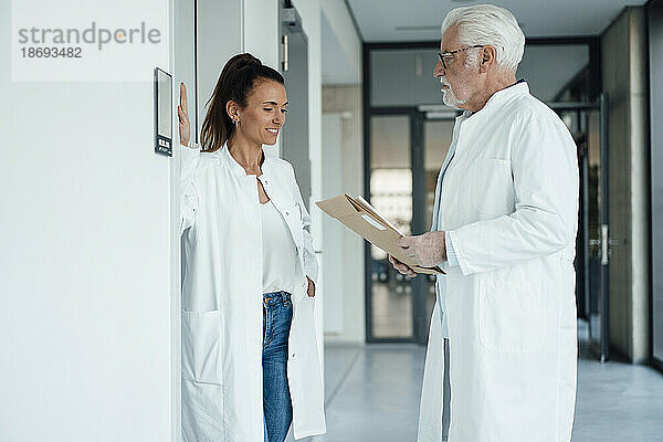 Lächelnder Arzt diskutiert mit einem älteren Kollegen  der im Krankenhaus ein Dokument hält