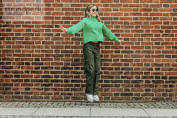 Teenage girl jumping in front of brick wall