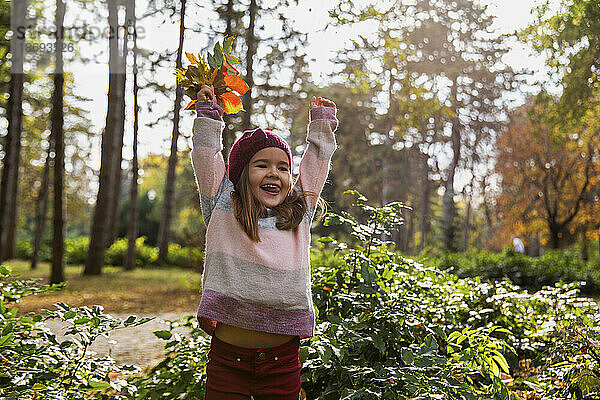 Fröhliches Mädchen  das im Park mit Blättern spielt