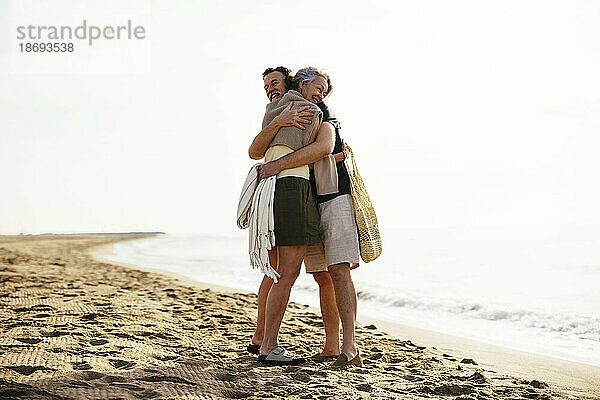 Reifer Mann umarmt Frau  die auf Sand am Strand steht