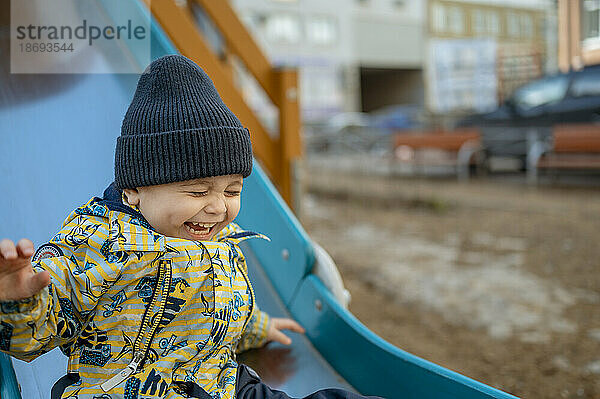 Cheerful boy enjoying on slide in playground