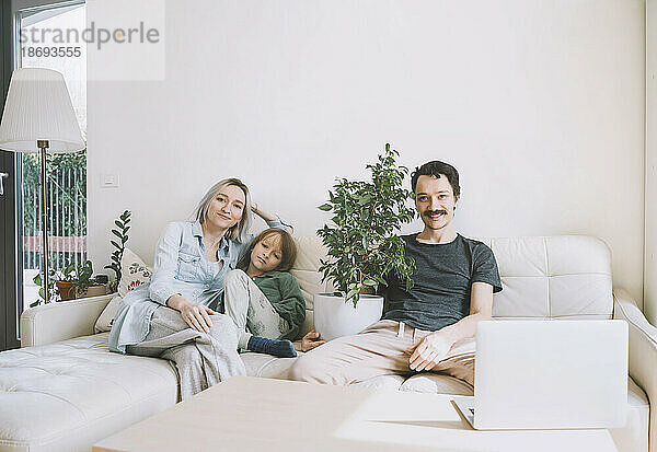 Lächelnder Mann und Frau sitzen zu Hause mit ihrem Sohn auf dem Sofa