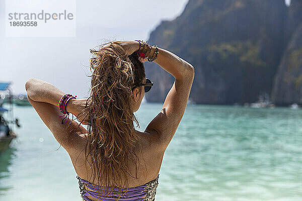 Frau mit der Hand im Haar blickt aufs Meer