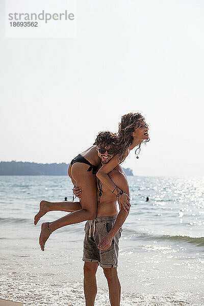 Mann trägt Freundin auf der Schulter am Strand