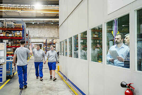Zufriedene Kollegen geben High-Five beim Spaziergang in der Produktionshalle der Fabrik