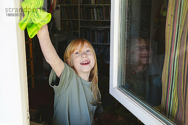 Lächelndes Mädchen putzt Fenster zu Hause