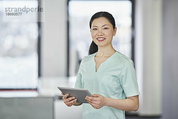 Porträt einer lächelnden Krankenschwester im Kittel  die ein digitales Tablet in der Hand hält