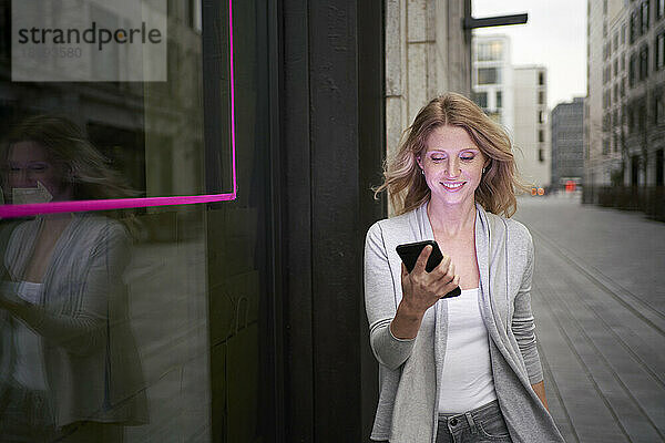 Blonde Frau benutzt Smartphone am Bürgersteig