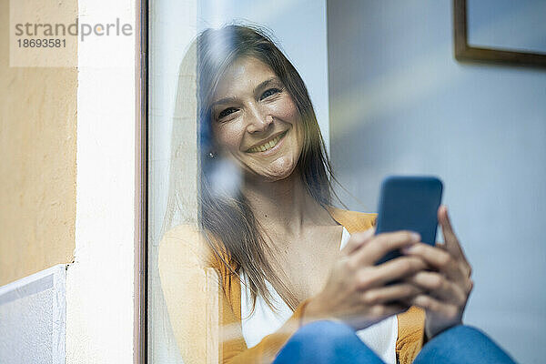 Glückliche Frau hält Smartphone im Café  gesehen durch Glasfenster