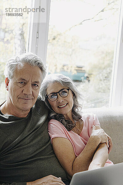 Porträt eines älteren Paares mit Laptop  das es sich zu Hause auf der Couch gemütlich macht
