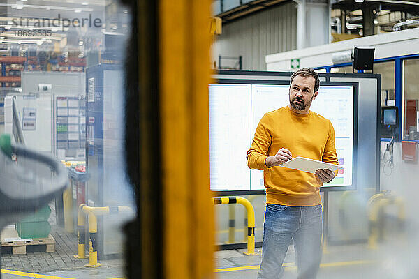 Nachdenklicher Mann steht mit Tablet-PC in der Fabrik