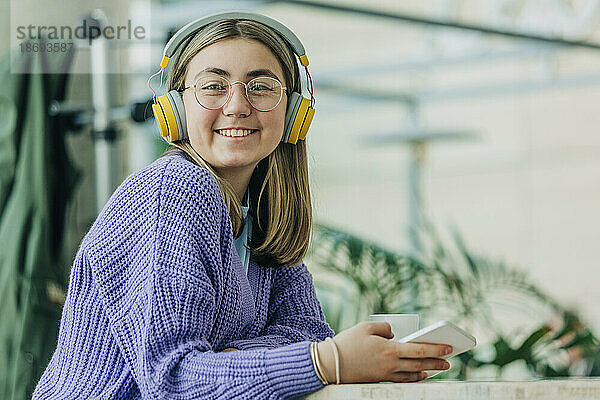 Glückliches Teenager-Mädchen mit Bluetooth-Kopfhörern in der Schulkantine