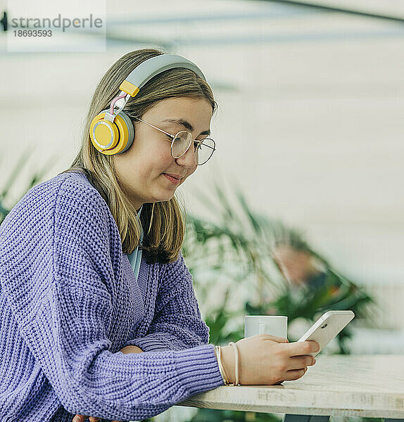 Lächelndes Mädchen  das in der Schulcafeteria Musik über drahtlose Kopfhörer hört