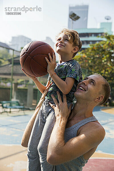 Glücklicher Vater mit Sohn  der an einem sonnigen Tag Basketball spielt