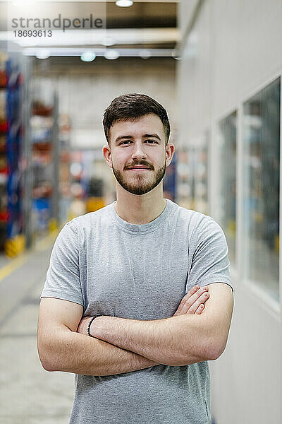 Smiling young employee with arms crossed standing at factory