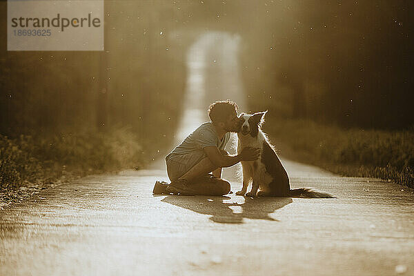 Junger Mann küsst Border-Collie-Hund auf der Straße bei Sonnenuntergang