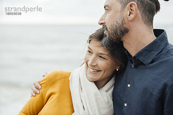 Glücklicher Mann umarmt Frau am Strand
