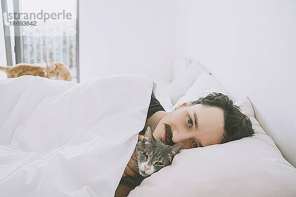 Lächelnder Mann entspannt sich zu Hause mit Katze im Bett