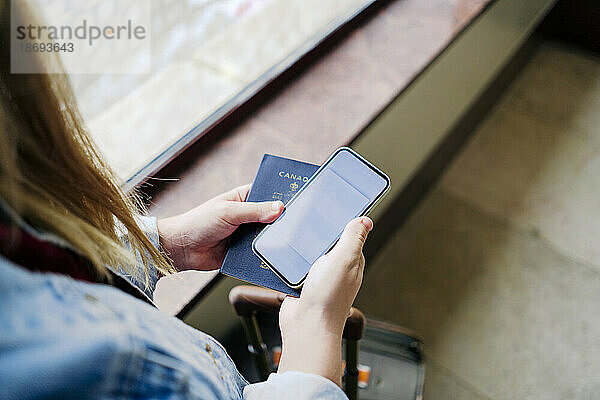 Frau hält Smartphone und Reisepass in der Hand