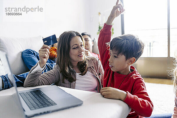 Mutter hält Kredit von Sohn mit erhobener Hand zu Hause am Laptop