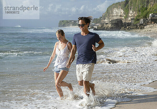 Glückliches junges Paar läuft am Strand im Meerwasser