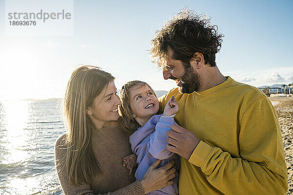 Lächelnde Tochter  die Spaß mit Vater und Mutter am Strand hat