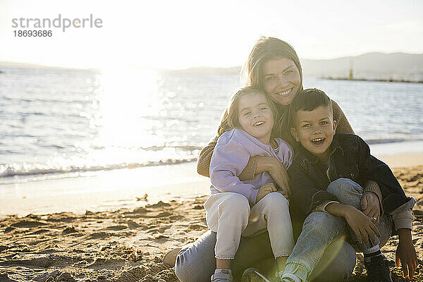 Lächelnde Frau sitzt mit Sohn und Tochter am Strand