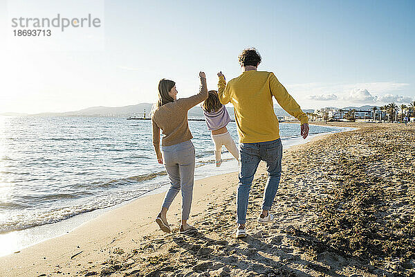 Vater und Mutter holen ihre Tochter hoch  die am Strand über den Sand spaziert