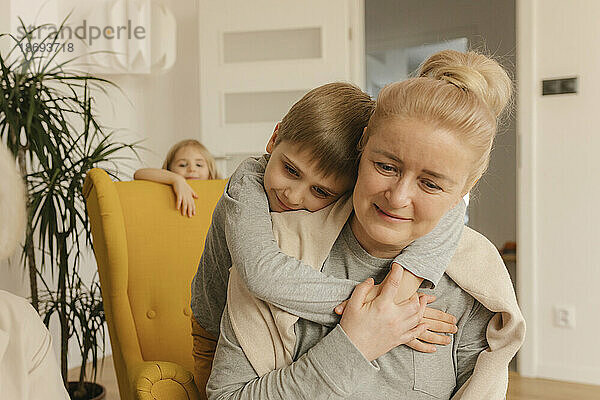 Junge umarmt Großmutter  die zu Hause sitzt