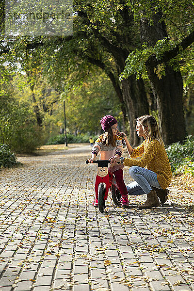Mutter hilft Tochter  die im Park auf dem Fahrrad sitzt