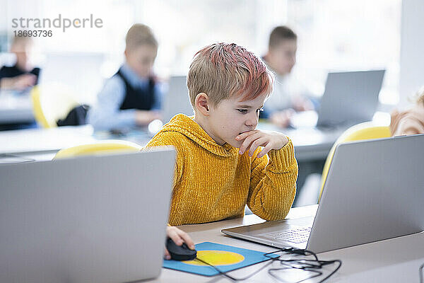Nachdenklicher Junge benutzt Laptop im Computerunterricht in der Schule