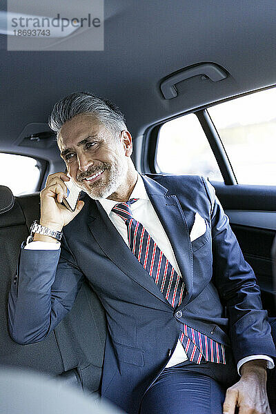 Lächelnder Geschäftsmann  der im Auto sitzt und auf dem Smartphone spricht
