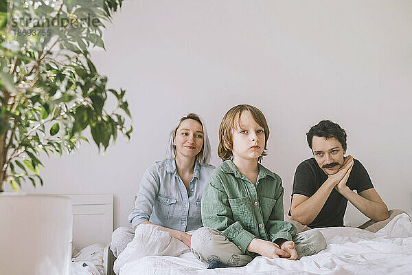 Lächelnder Mann und Frau mit Sohn sitzen zu Hause im Bett