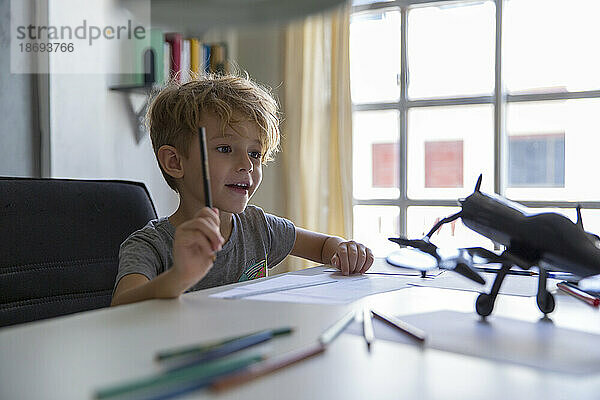 Überraschter Junge mit Bleistift blickt auf Modellflugzeug